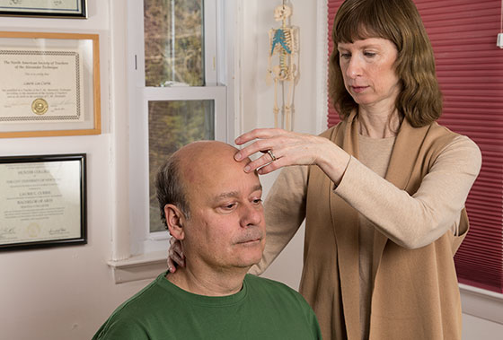 Certified Alexander Technique teacher Laurie Currie working with student's head/neck balance while seated in chair in Mahopac, New York.